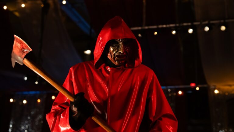 Horror movie villain. Scary masked figure in red raincoat holding bloody axe. Halloween horror concept.