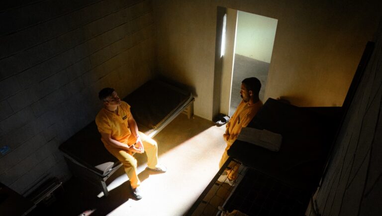 Two prisoners in a jail cell, wearing orange jumpsuits. Prison, jail, inmates.