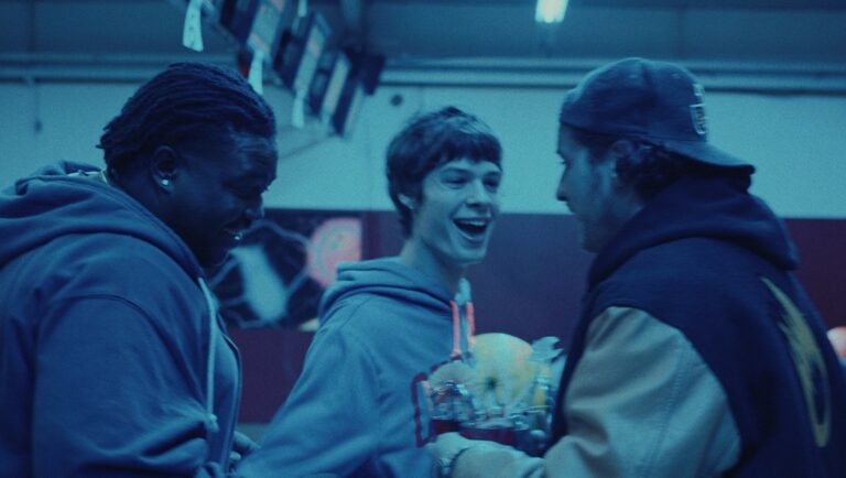 Three young men in hoodies, one laughing, hold a trophy. Meteors movie scene.