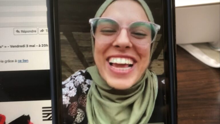 Smiling woman in hijab and glasses on a phone screen. Video call.