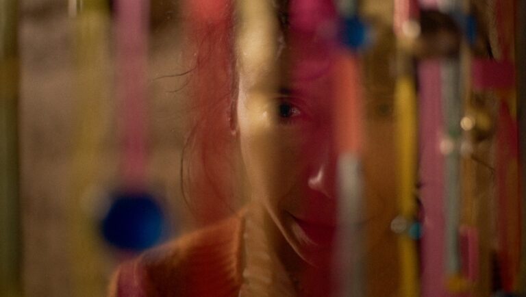 Close-up of a woman's face partially obscured by colorful, blurred decorations. Mysterious and artistic.