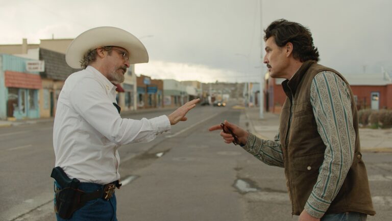 Eddington movie scene: Two men face off in a Western town street. One wears a cowboy hat and gun.