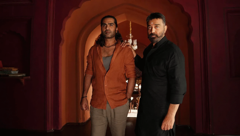 Two men, one with his hand on the other's shoulder, stand side by side and look offscreen.