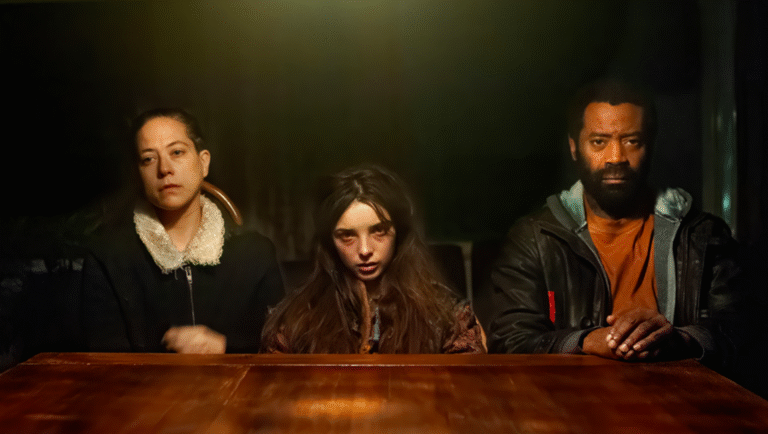 A woman, man, and young girl sitting at a table, staring straight ahead.
