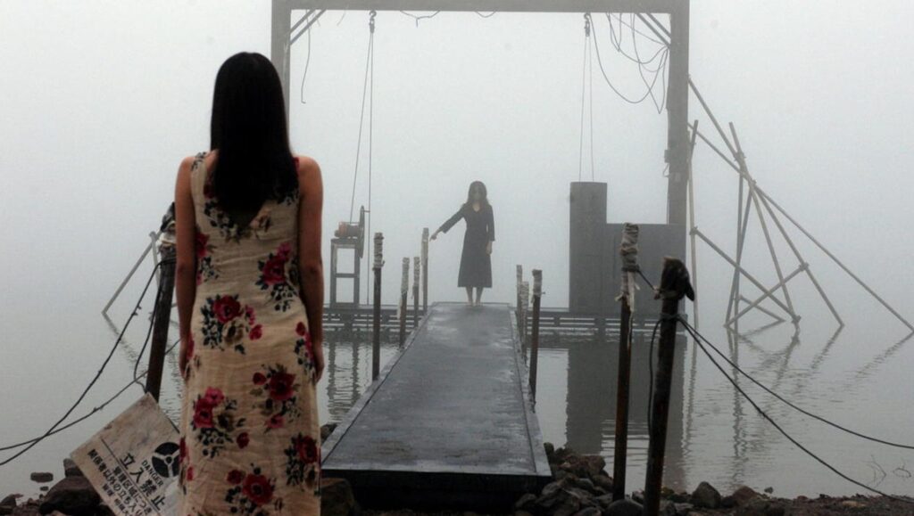 A woman looks toward the end of a dock where another woman stands in the distance.