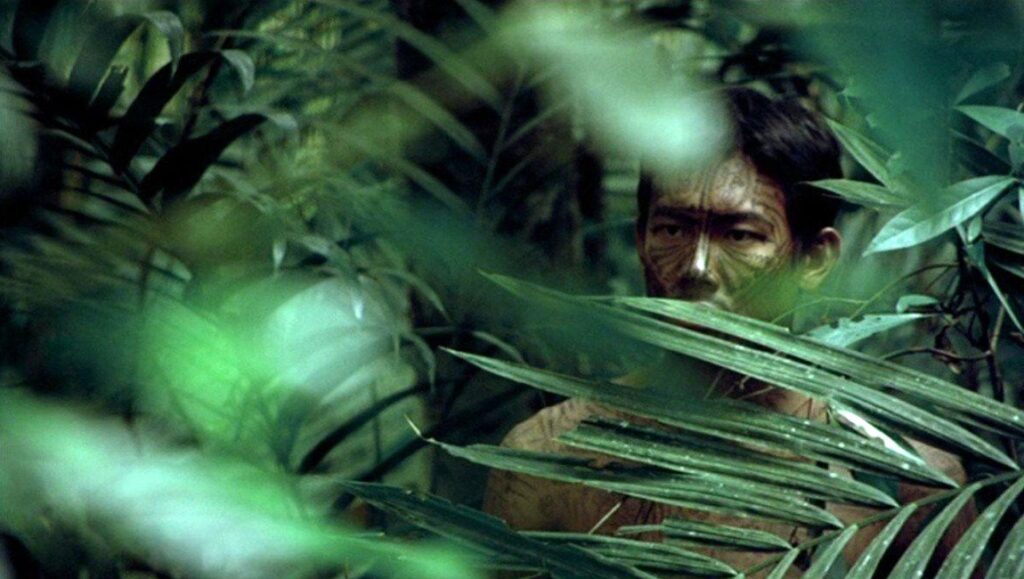 A man hidden in the jungle looks through branches.