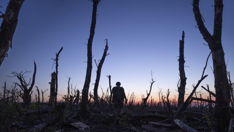 War in Andriivka: Soldier silhouette amidst charred trees at dusk. Ukraine conflict.