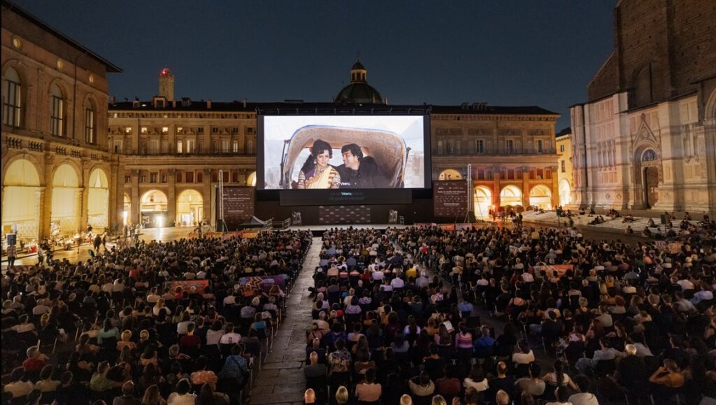 Il Cinema Ritrovato 2025 film festival in Piazza Maggiore, Bologna. Crowd watching outdoor movie screen at night.