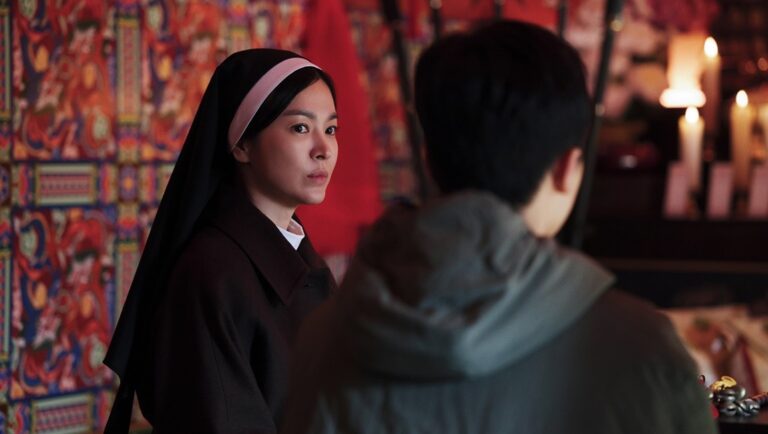 Still from Dark Nuns featuring a nun in a black habit looking intently at a person in a gray jacket. Candles in the background.