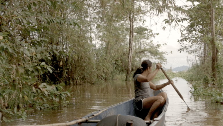 Film still from Bulakna at FIDMarseille 2025. Woman rows a boat through a lush, green waterway in the Philippines. WIP film.