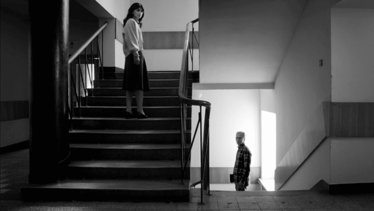 Black and white film still from FIDMarseille 2025 film Miraculous Accident. Woman on stairs, man below.