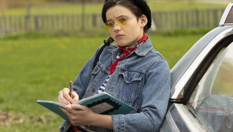Actor Dominic Sessa as Sal Price in Going Home. Sessa writes in a notebook, wearing yellow glasses and a denim jacket.