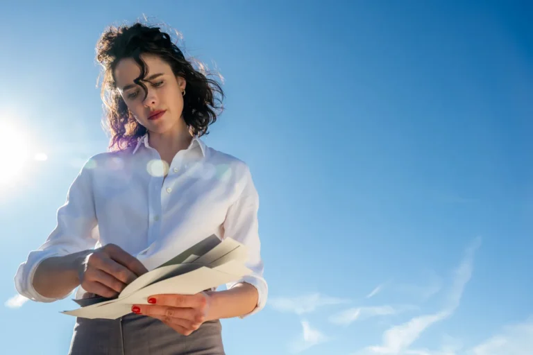 Woman in white shirt reads documents against a blue sky. Businesswoman reviewing paperwork.