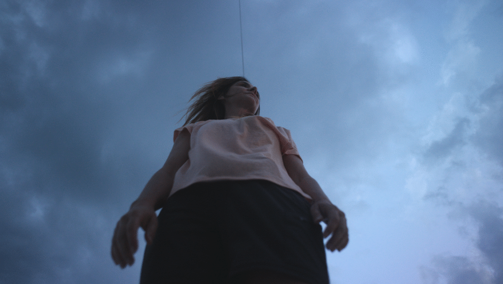 Woman looks up at cloudy sky. Low angle shot of female figure. Outdoors.