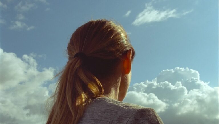 Woman looking at blue sky with clouds. Ponytail hairstyle. Back view. Dreamy.
