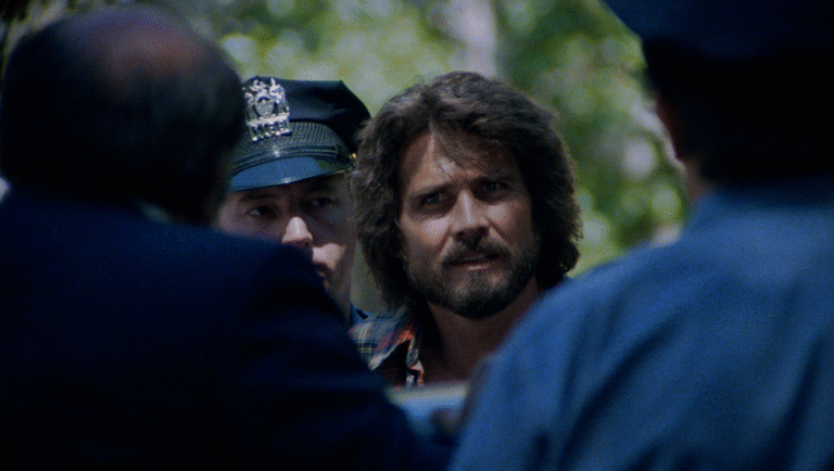 Night of the Juggler movie scene: a man with a beard and long hair is flanked by two police officers.
