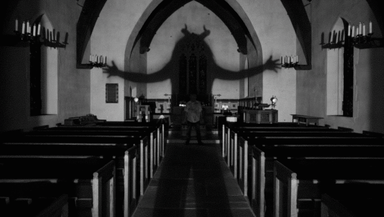 Black and white horror scene. A man stands in a church with a devil shadow on the wall.