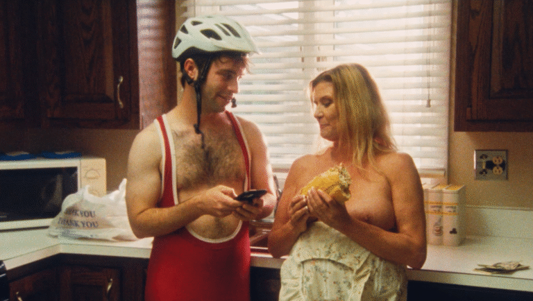 Kitchen scene with a cyclist in a helmet using a phone and a topless woman holding a sandwich.