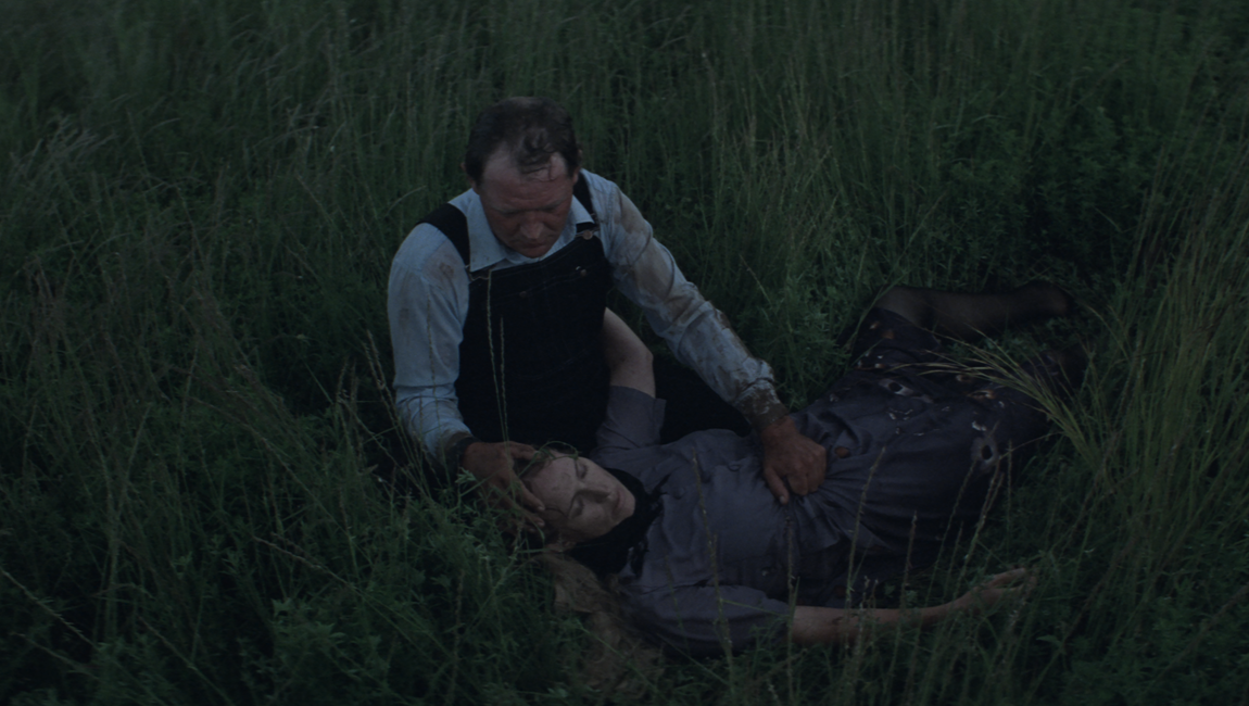 Man cradling injured woman in field. Dark, cinematic scene. Silent Light film still.