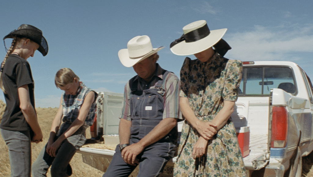 Amish family portrait. Farmers with hats and traditional clothing stand by a pickup truck in a rural setting.