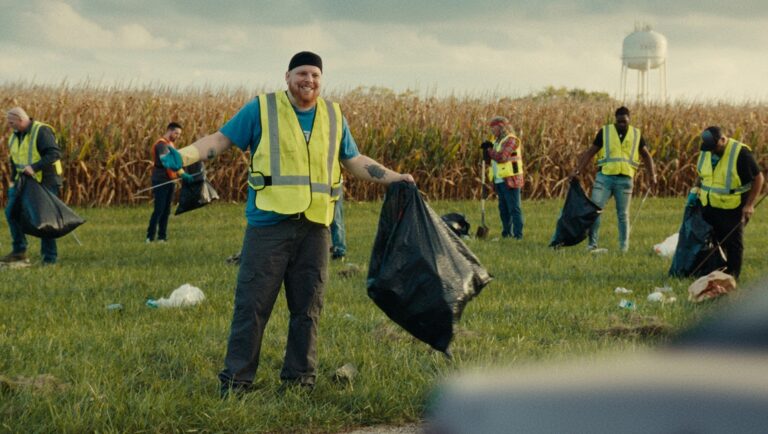 Volunteers clean up litter along roadside. Community cleanup event. Environmental awareness, teamwork. Black trash bags, safety vests.
