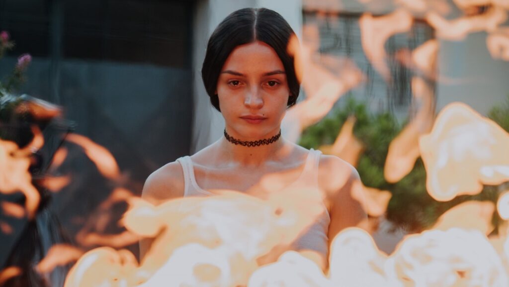 Young woman in a choker necklace with flames in the foreground. Fire aesthetic.