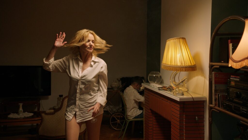 Scene from Un balcon à Limoges film. Woman in shirt, man at desk, vintage interior.