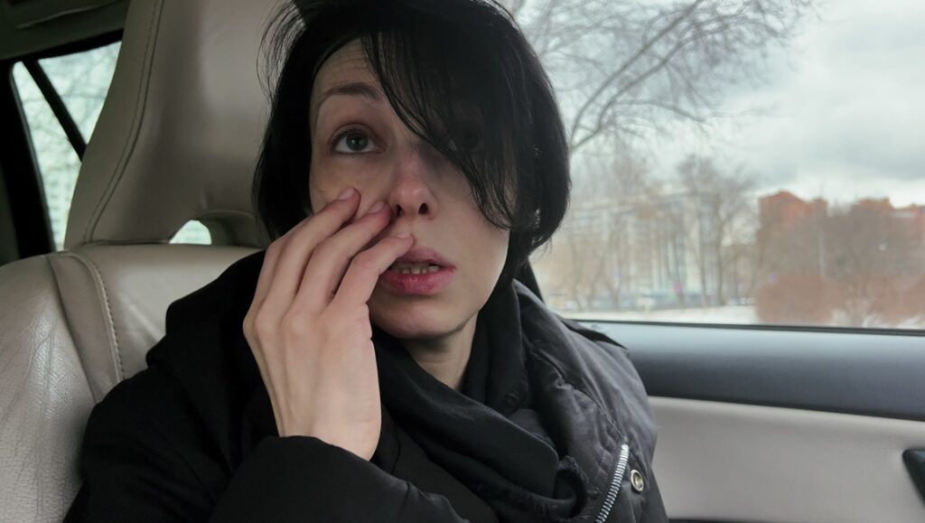 Woman in car. Emotional distress, wiping tears. Black hair, winter coat. Sadness, vulnerability.