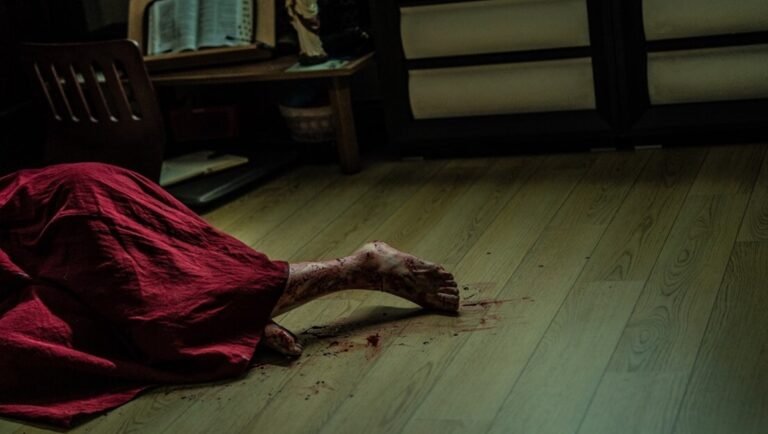 Horror scene: Body covered in red fabric, bloody foot on wood floor. Crime scene, mystery.